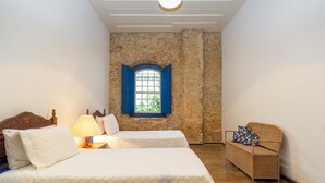 A bedroom with two beds, a window with blue shutters, a wicker sofa, and a lamp. - Historic house in the center of Paraty, with incredible sea views. (Paraty)