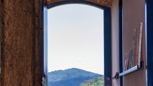 A hallway leading to a beach view with a stone wall, a metal door, and a hanging light fixture. - Historic house in the center of Paraty, with incredible sea views. (Paraty)