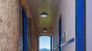 A corridor with stone walls, wooden flooring, and blue doors leading to a room with a view of the landscape. - Historic house in the center of Paraty, with incredible sea views. (Paraty)