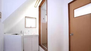 A narrow hallway with a wooden door, a white sink, and a mirror on the wall. - GORAKU Shinfukae 201 (Osaka)