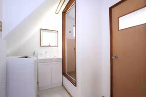 A narrow hallway with a wooden door, a white sink, and a mirror on the wall. - GORAKU Shinfukae 201 (Osaka)