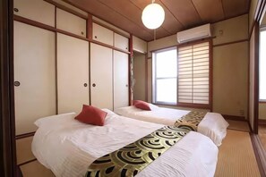 A traditional Japanese-style room with tatami flooring, two beds with red pillows, a shoji screen, and a hanging light fixture. - GORAKU Shinfukae 201 (Osaka)