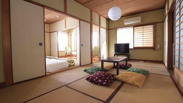 A traditional Japanese room with tatami flooring, sliding doors, a television, and a bed. - GORAKU Shinfukae 201 (Osaka)