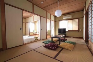 Une pièce de style japonais traditionnel, avec un sol recouvert de tatamis, des portes coulissantes, une télévision et un lit.