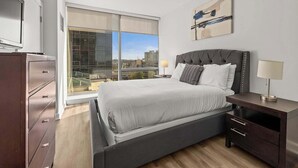 Une chambre moderne avec un grand lit, une table de chevet, une commode et une fenêtre donnant sur la ville.
