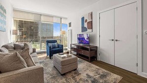 Un salon moderne avec un canapé, un pouf et un téléviseur posé sur un meuble.