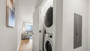 Une buanderie équipée d’un lave-linge et d’un sèche-linge, une porte donnant sur un balcon et un tableau accroché au mur.