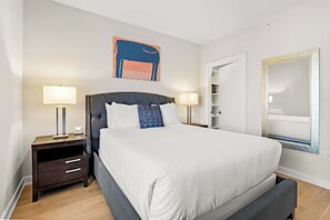 Moderni hotellihuone, jossa on suuri sänky, kaksi yöpöytää valaisimineen, vaatekaappi ja suuri peili.
