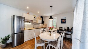 A modern kitchen with a stainless steel refrigerator, white cabinets, and a dining area with a round table and chairs. - MAB Sweet Home By Villas Guide (Vela Luka)
