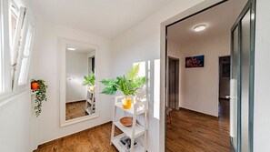 A hallway with a wooden floor, white walls, a mirror, and potted plants.