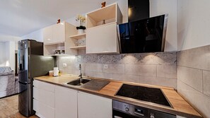 A modern kitchen with a built-in oven, a stainless steel refrigerator, and a wooden countertop.