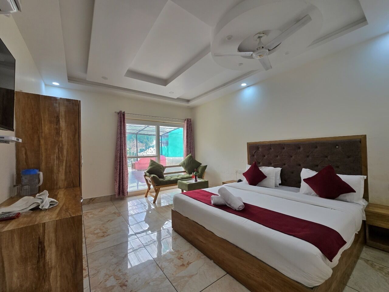 A hotel room with a large bed, a wooden wardrobe, a small table, and a view of the outdoors.
