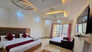 A hotel room with a large bed, a sofa, a coffee table with a bottle and glass, and a TV mounted on the wall. - Hotel New Snow Palace  (Dharamshala)