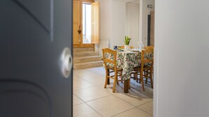 A dining area with a table set for four, surrounded by wooden chairs, a potted plant, and a window with open shutters. - La Casa del Nostromo (Salerno)
