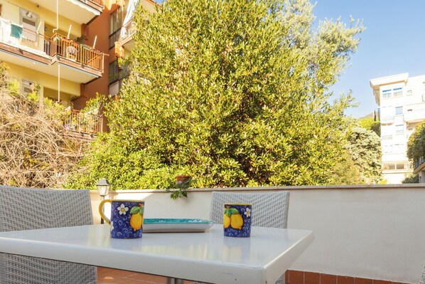Un balcón con mobiliario de mimbre, una mesa y dos tazas decorativas.