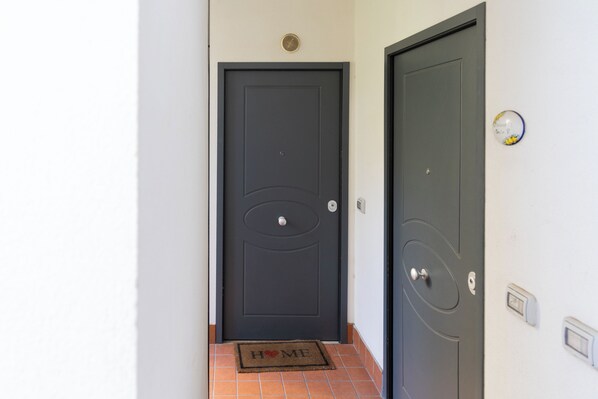 Una puerta gris oscuro con un felpudo que dice 'HOME' y una pequeña placa circular en la pared a la derecha.