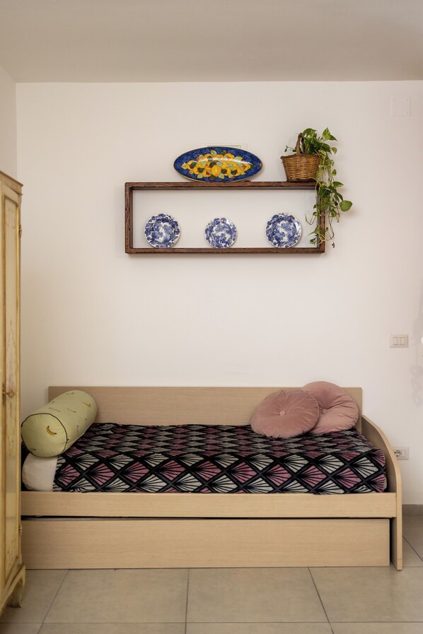 Una habitación pequeña y acogedora con una cama de madera, un estante con platos decorativos y una planta en maceta.