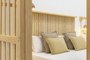 Un lit avec une tête de lit en bois, plusieurs oreillers et un luminaire fixé au mur.
