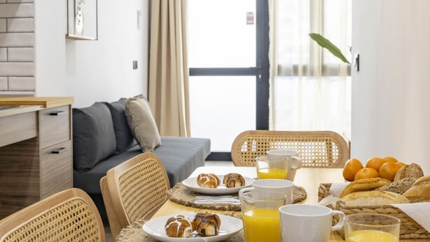 A breakfast setup with croissants, orange juice, and bread on a table in a room with a sofa and wicker chairs. - Travel Habitat Nou Mestalla 6 (Valencia)