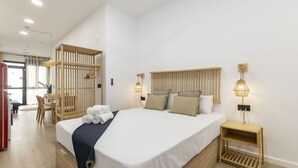 A modern hotel room with a large bed, wooden headboard, bedside tables, and a seating area with a table and chairs. - Travel Habitat Nou Mestalla 6 (Valencia)