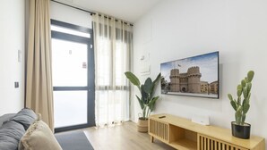 A modern living room with a sofa, a wooden console table, a large window with sheer curtains, and a cactus plant. - Travel Habitat Nou Mestalla 6 (Valencia)