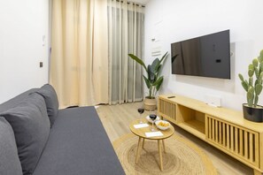 Un salon moderne avec un canapé gris, une table basse en bois sur laquelle se trouvent un bol et des verres, un téléviseur fixé au mur et une plante en pot.