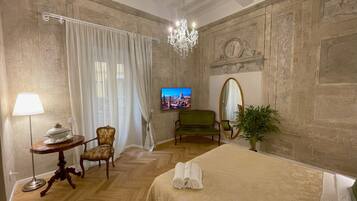 A hotel room with a bed, a television, a mirror, a chair, a table, and a plant.