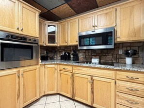 A kitchen with wooden cabinets, a microwave, an oven, and a stone backsplash. - Sleeps 30 • Theater • Game Room • Big Cedar Area (Ridgedale)