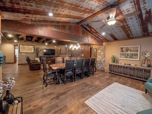 A rustic dining area with a wooden table and chairs, a television, and a stone wall with a sign. - Sleeps 30 • Theater • Game Room • Big Cedar Area (Ridgedale)