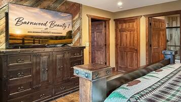 Ein Schlafzimmer mit großem Holzschrank, einem Bett mit gemustertem Überwurf und einem Fernseher, der 'Barnwood Beauty 1' anzeigt.