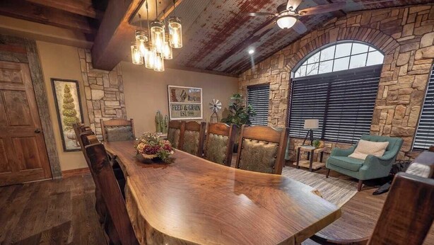 A rustic dining area with a large wooden table, stone walls, and a stone fireplace. - Sleeps 30 • Theater • Game Room • Big Cedar Area (Ridgedale)
