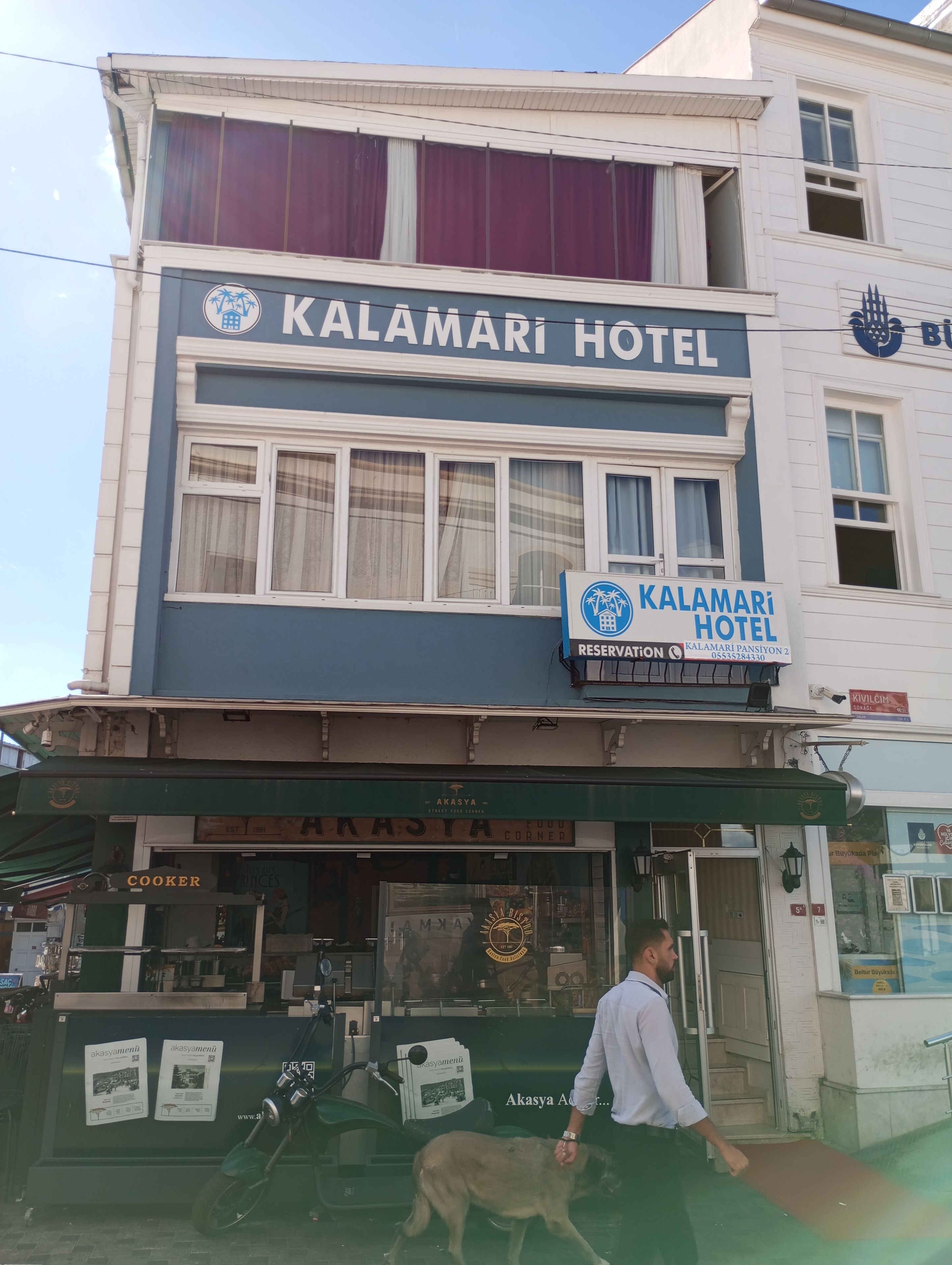A hotel named 'Kalamari Hotel' with a signboard indicating a reservation number and a contact number.