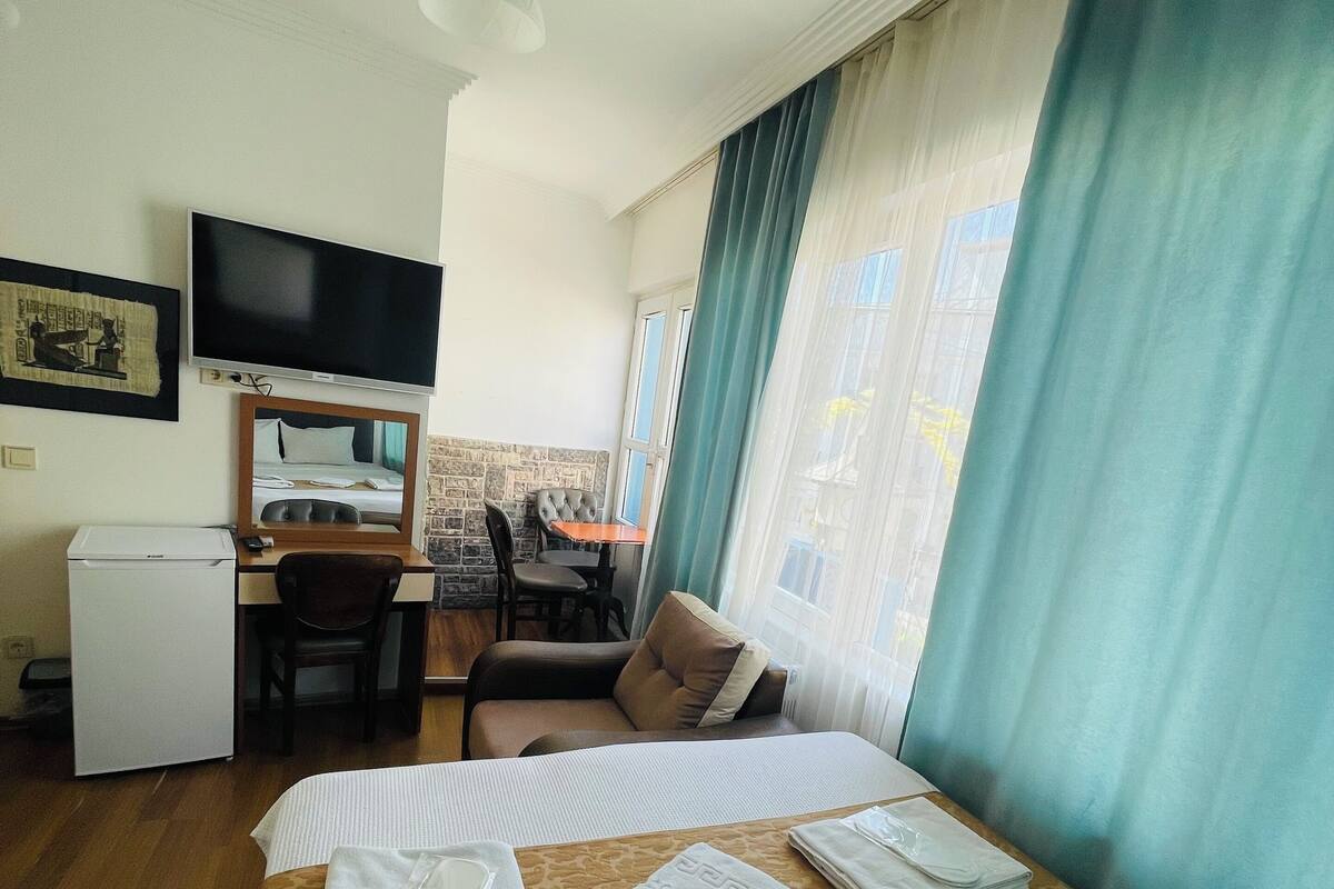 A hotel room with a bed, a desk, a chair, a television, and a window with curtains.