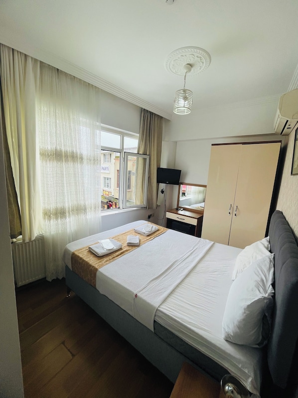 A hotel room with a bed, a wardrobe, a desk with a chair, a window with curtains, and a radiator. - Kalamaripansiyon2 (Adalar)
