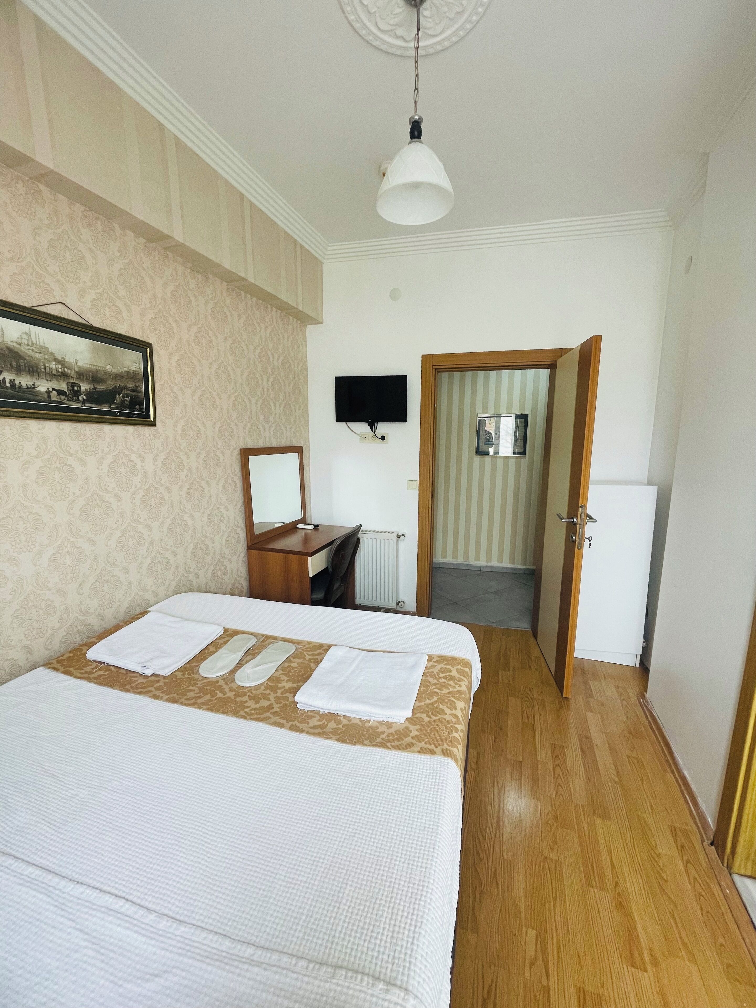 A hotel room with a bed, a desk, a chair, a television, and a door leading to another room.
