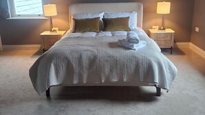 Un dormitorio con una cama grande, dos lámparas de noche, una ventana con persianas y dos cuadros en la pared.
