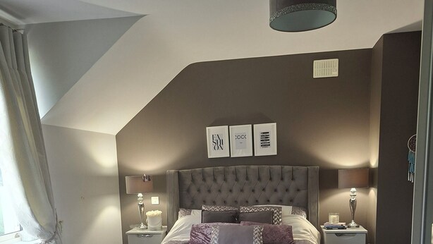 Une chambre à coucher avec un grand lit, deux tables de chevet, un luminaire au plafond et une fenêtre avec des rideaux.