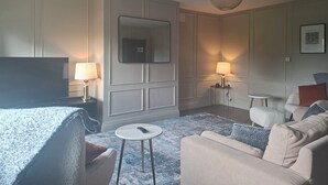 Une chambre d’hôtel moderne avec un grand lit, une télévision, deux lampes de chevet, une table ronde, un canapé et un luminaire suspendu.