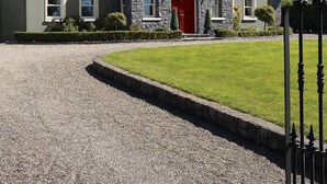 Une maison en pierre avec une porte rouge, une allée en gravier et une pelouse bien entretenue.