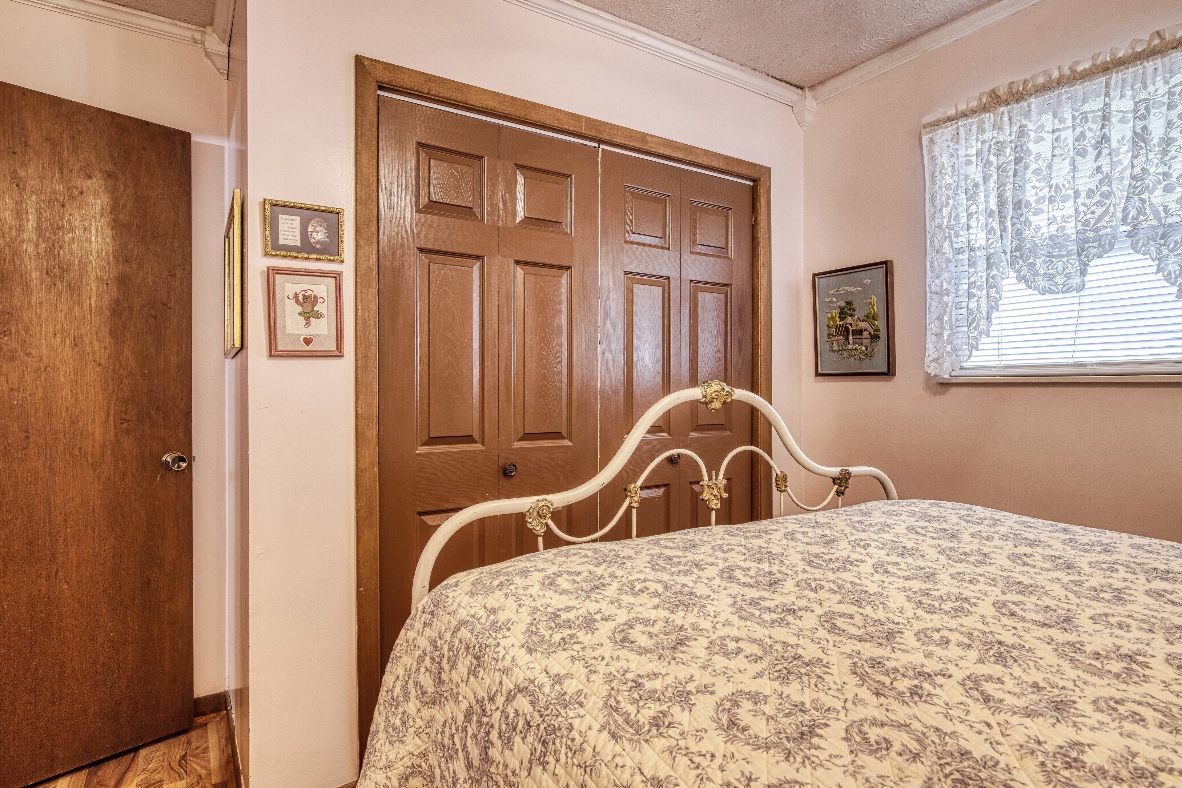 A bedroom with a wooden door, a bed with a floral bedspread, and a window with lace curtains.