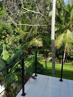 A balcony with a metal railing overlooking a lush garden with various tropical plants and a palm tree. - Colombo Airport Field View Villa (Andiambala)