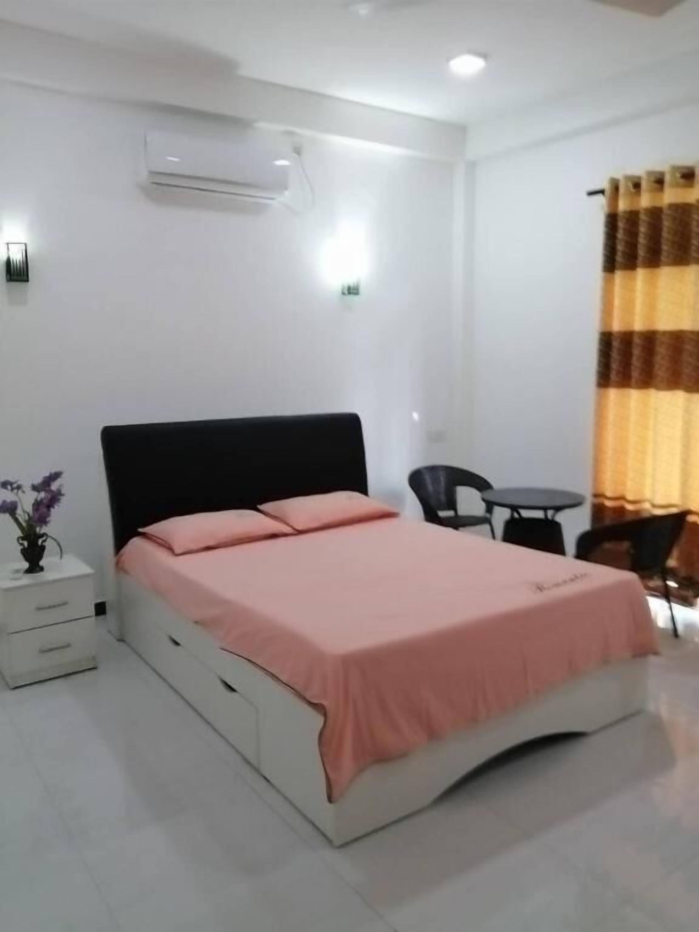 A bedroom with a bed, a bedside table, a chair, a small table, and a curtain.