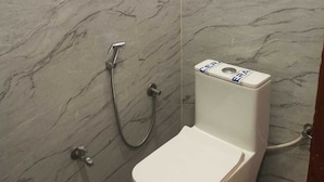 A bathroom with a toilet, a shower, and a marble wall. - Hotel Parents Inn (Prayagraj)