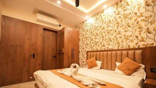 A hotel room with a wooden wardrobe, a bed with a swan-shaped towel, and a patterned wallpaper. - Hotel Parents Inn (Prayagraj)