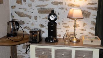 Ett litet kök med en kaffebryggare, brödrost och en lampa placerade på ett träbord framför en stenmur.