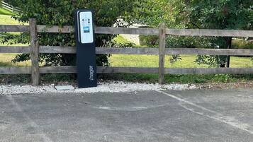 Un espace de stationnement équipé d’une borne de recharge portant l’inscription « Hager », situé près d’une clôture en bois et d’une zone verdoyante.