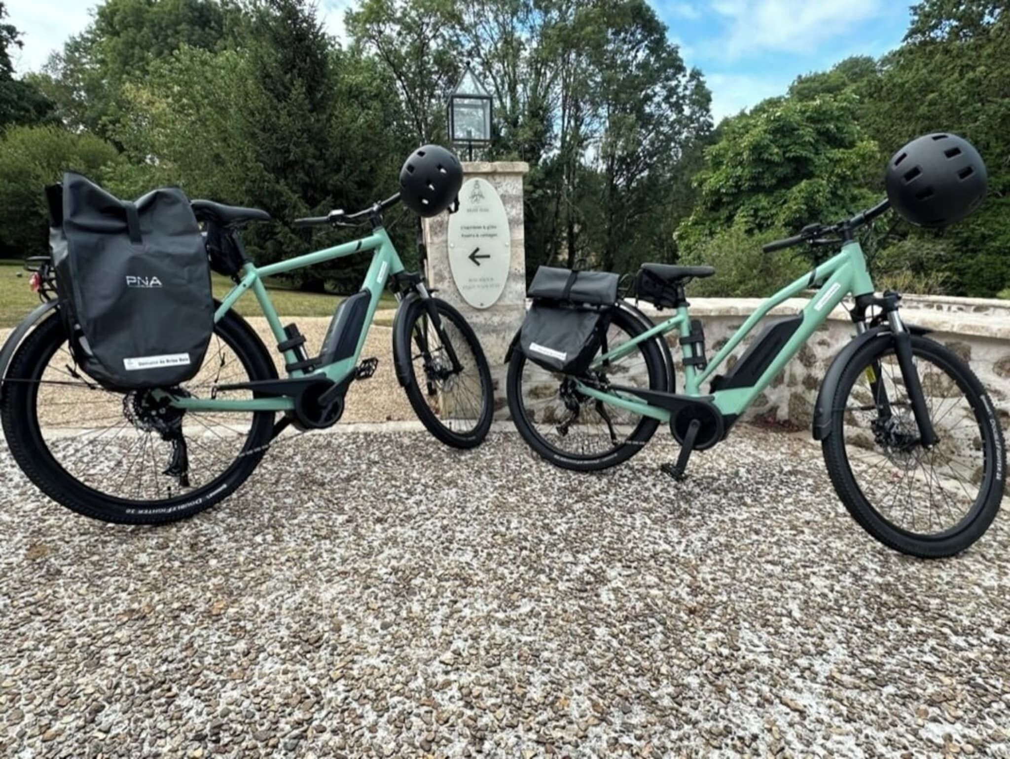 Zwei E-Bikes auf einem Kiesweg, im Hintergrund eine Steinmauer und Bäume.