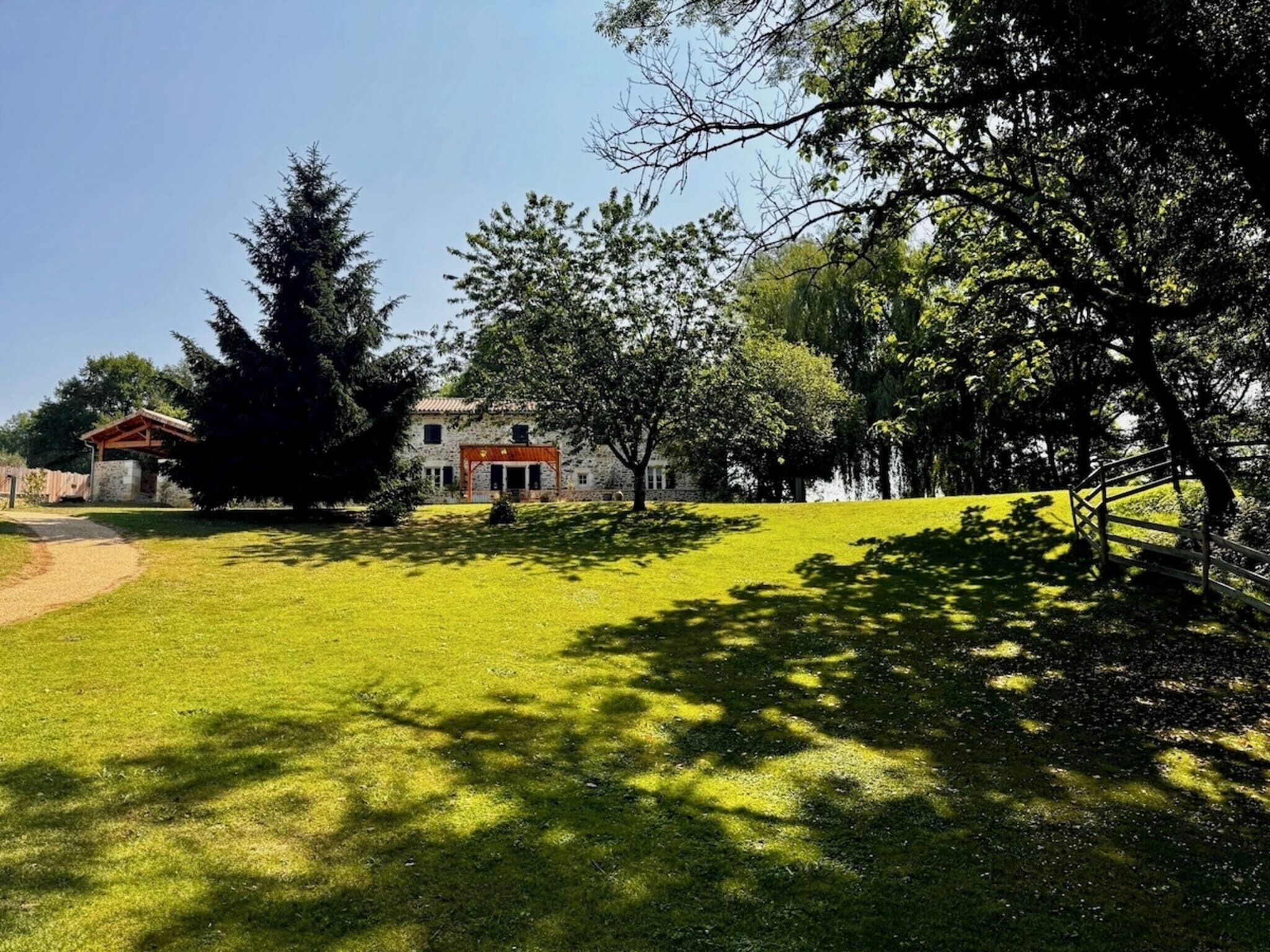 A well-maintained grassy area with a stone building, a wooden pergola, and a wooden fence.