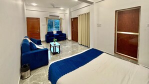 A hotel room with a large bed, a blue sofa, a small table with a plant, and a ceiling fan. - Zuna Stayz Morjim Goa (Morjim)