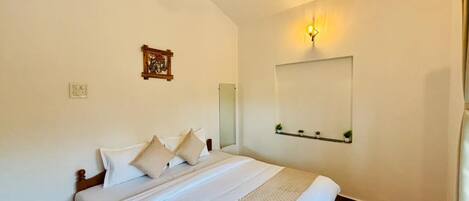 A bedroom with a bed, a ceiling fan, a wall-mounted light, and a small shelf with plants.